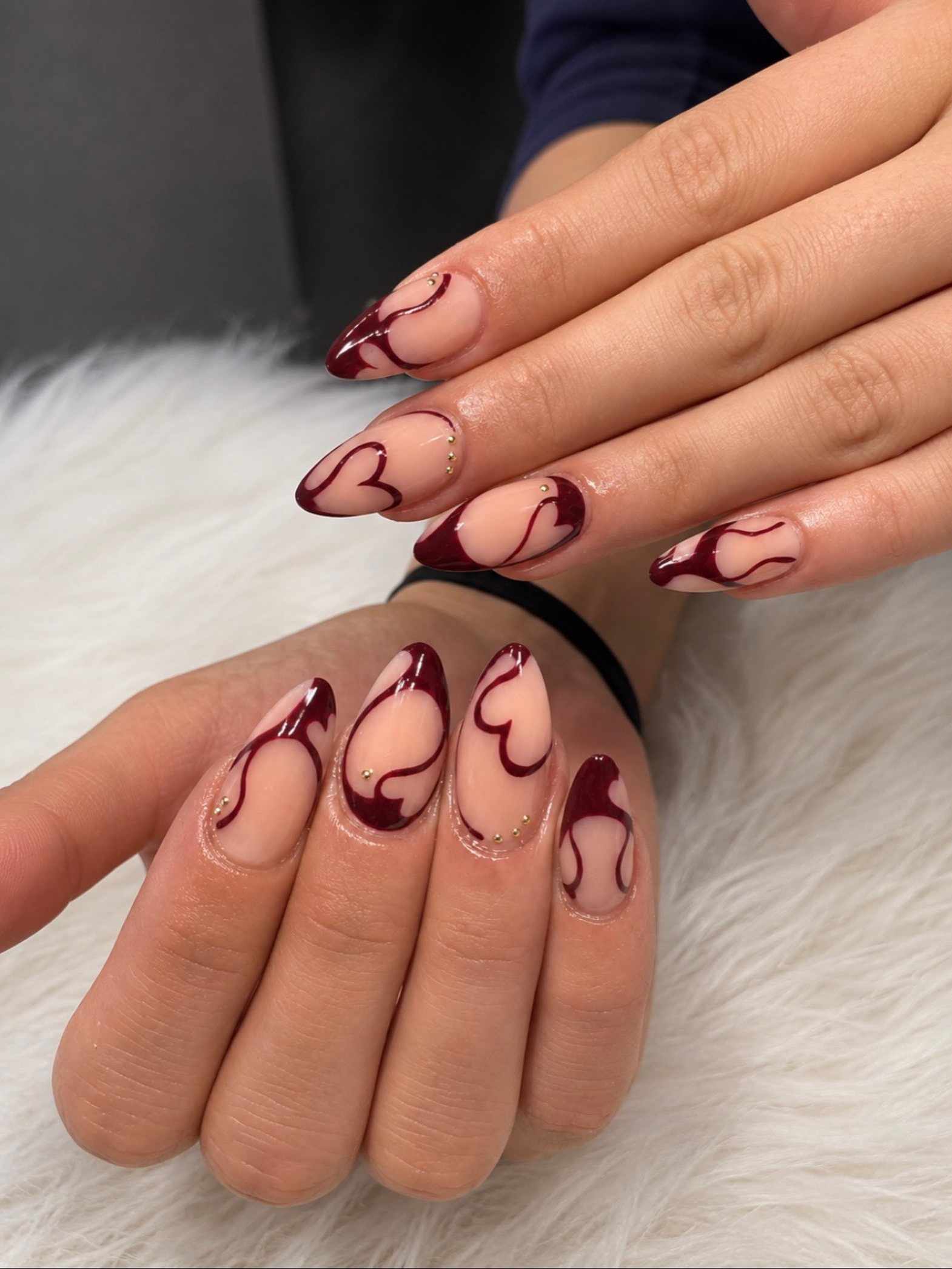 Nude amandelnagels met donkerrode hartjes en swirls